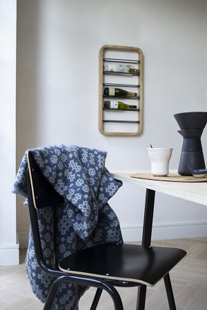 Chair with a floral-patterned cover, table with a vase, and wall-mounted shelf with bottles in a room.