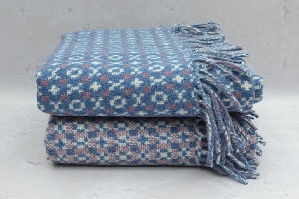 Gorwel Welsh Blanket. Stack of blue patterned blankets with tassels on a light gray background